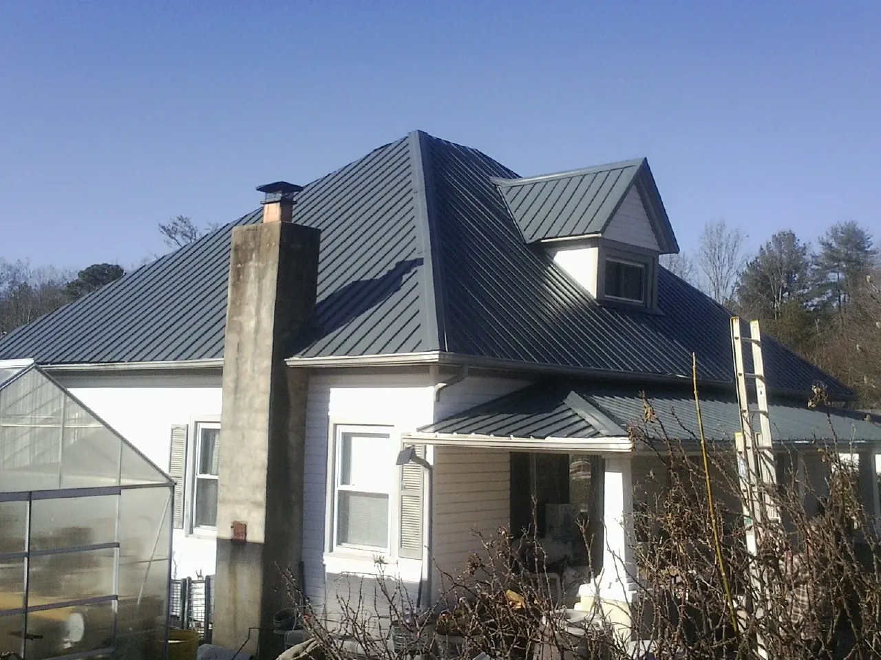 Dark blue standing seam metal roof on a white farmhouse with dormer — Slate & Tile Roof Repair by Roofing Brothers in Bedford Hills
