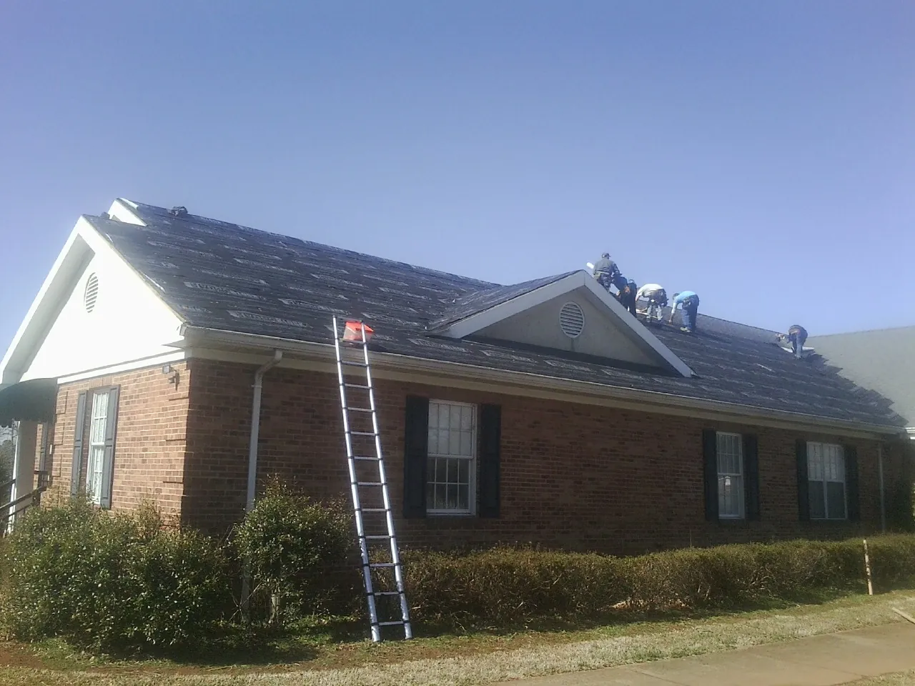Crew tearing shingles off a brick ranch roof with a ladder set — Metal Roof Repair work by our crew in Bedford Hills