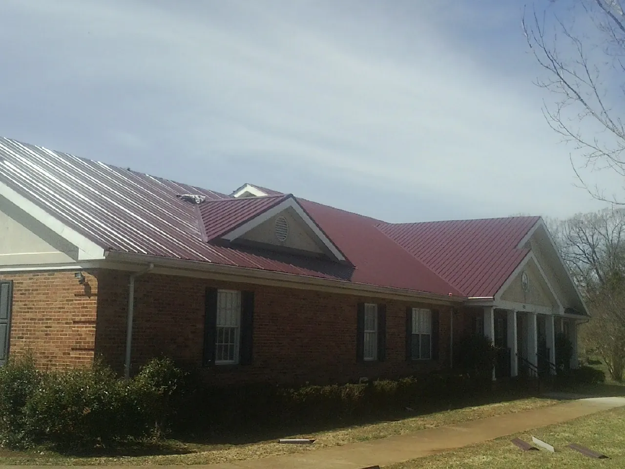 Red metal roof with gabled entries on a long brick building, from a Hail Damage Roof Repair job in Bedford Hills