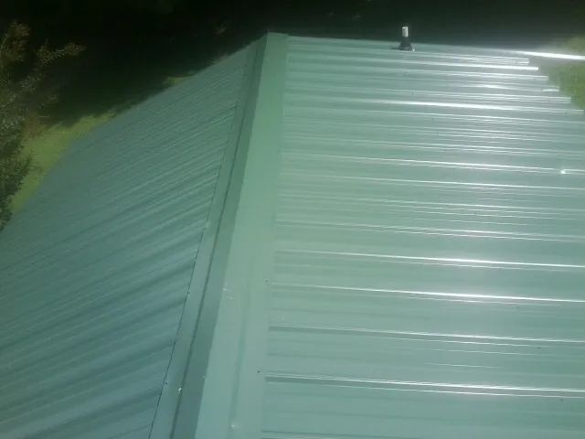 New green metal panels meeting at the ridge of a roof — Flat Roof Repair work by our crew in Bedford Hills