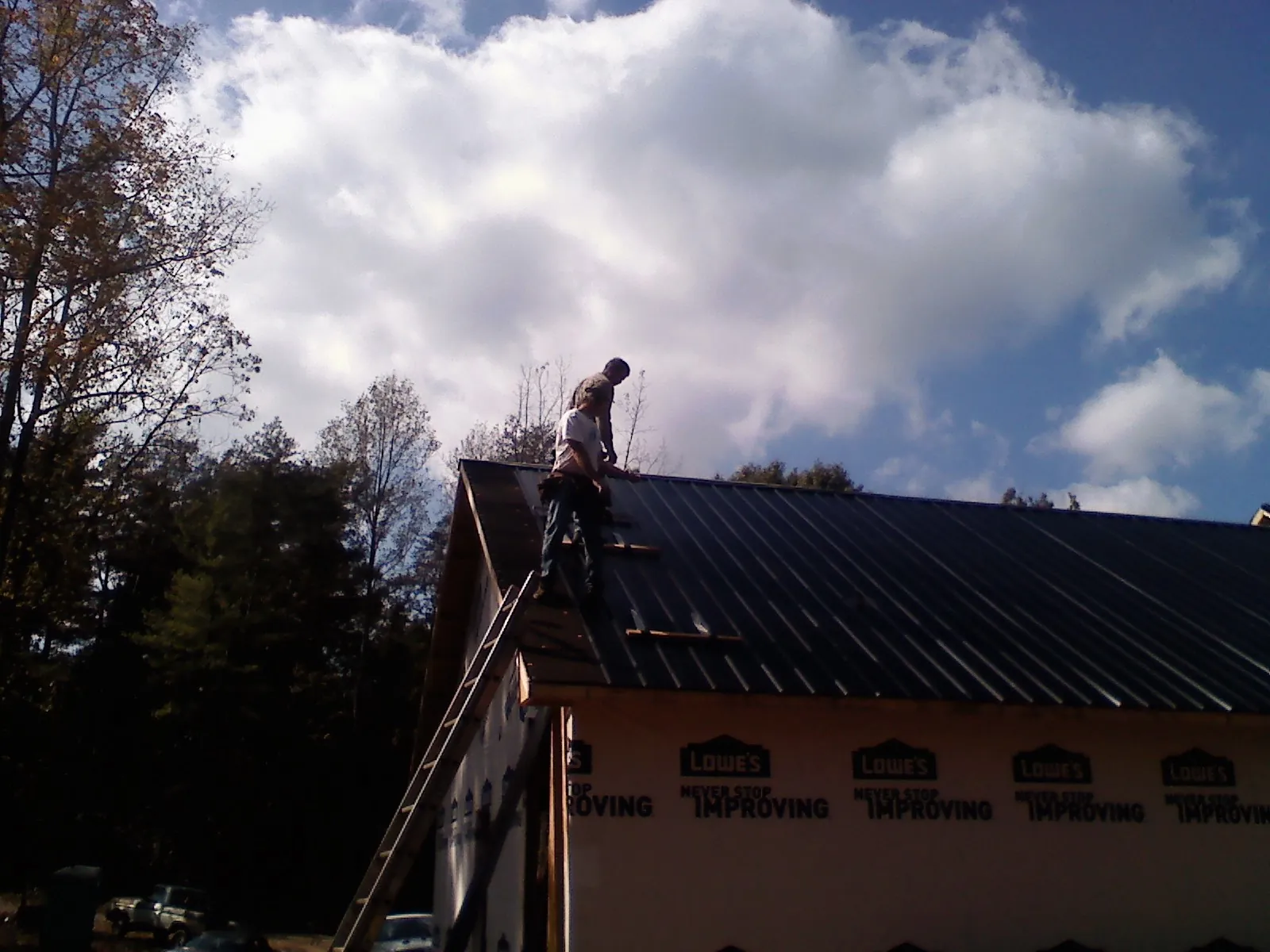 Roofer fastening dark metal panels high against a cloudy sky, from a Roof Inspection job in Bedford Hills