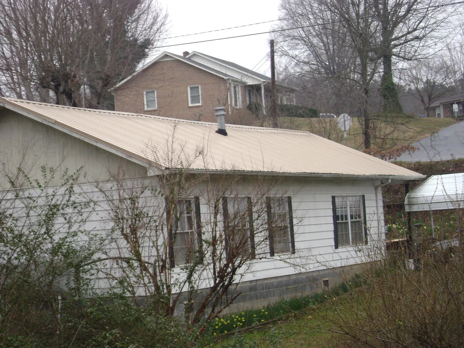 Tan metal roof on a white sided house set into a hillside — Commercial Roofing by Roofing Brothers in Bedford Hills