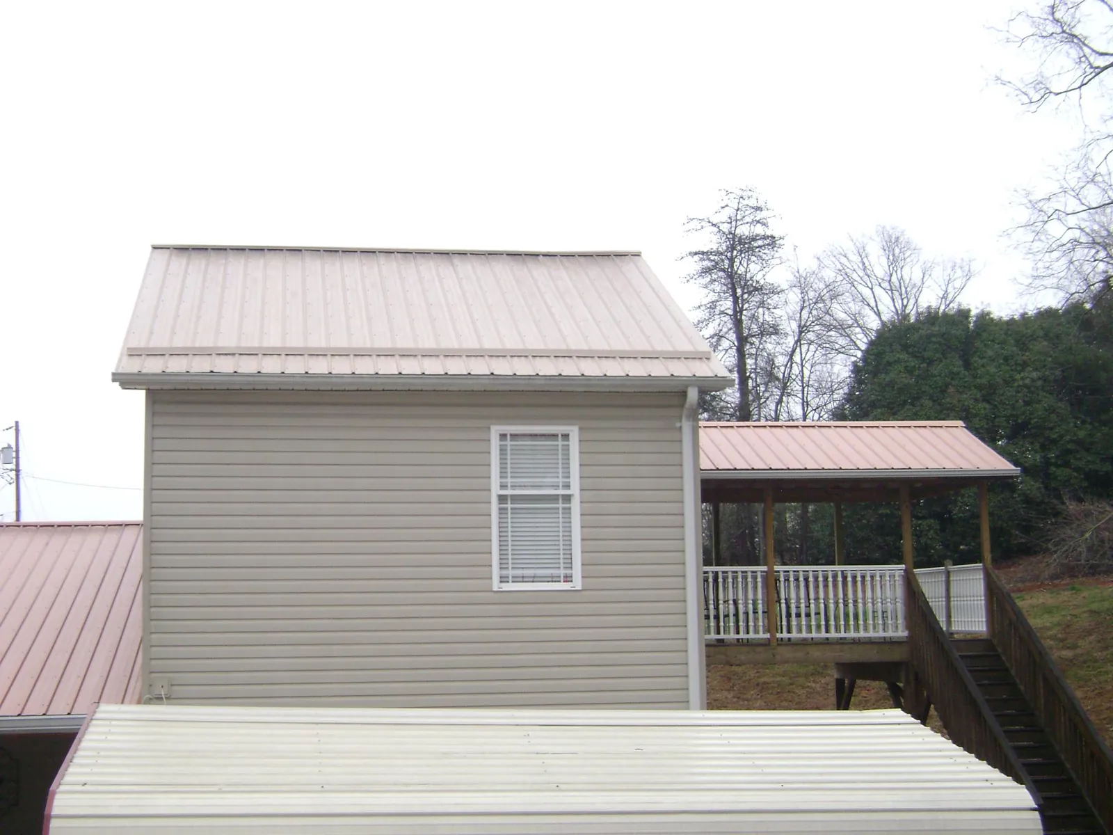 Tan metal roofs on a two story addition and attached porch, from a Roof Replacement job in Bedford Hills