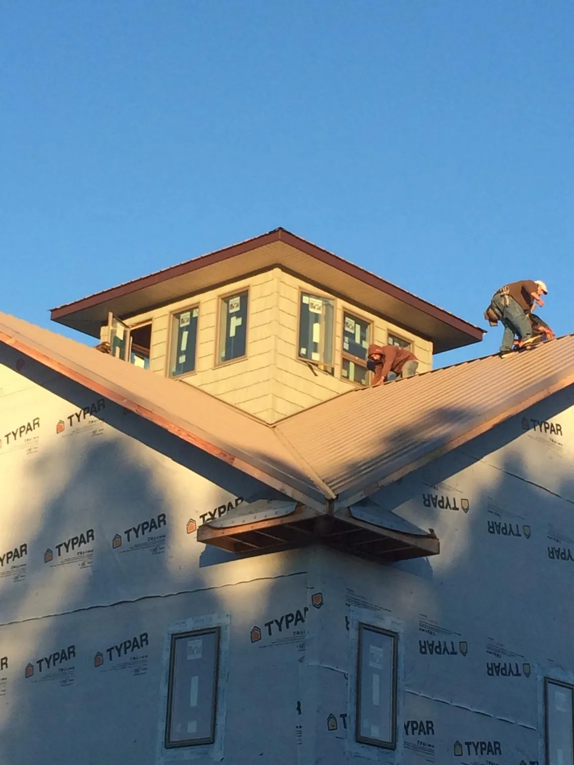 Roofers working around a rooftop cupola on a new metal roof at sunset — Roof Waterproofing in Bedford Hills by Roofing Brothers